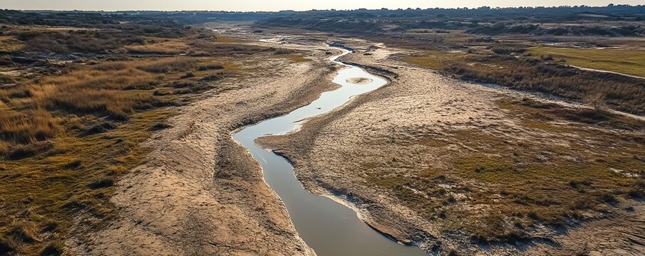 Aerial view of a dry riverbed twisting through a barren landscape, showcasing the effects of drought in an expansive, parched area.