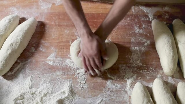 A skilled baker's hands expertly mold dough into a loaf shape on a rustic workbench