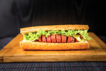 Hot Dog Sausage Sandwich with Cheese, Lettuce, and Tomato isolated on wooden board side view of breakfast on dark background