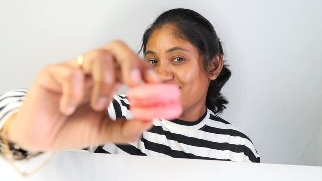 An indian women eating pink macaroons in white background