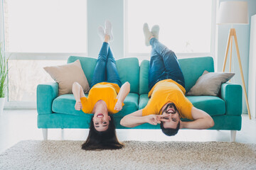 Full size photo of two young partners upside down couch v-sign raise fists free time modern interior apartment indoors