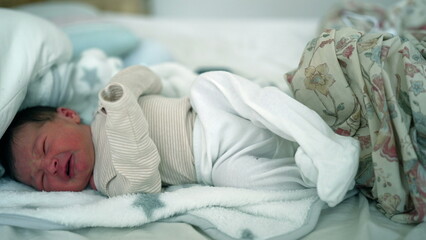 Newborn baby crying in bed, swaddled in a blanket, clearly in distress. a raw and emotional moment,...