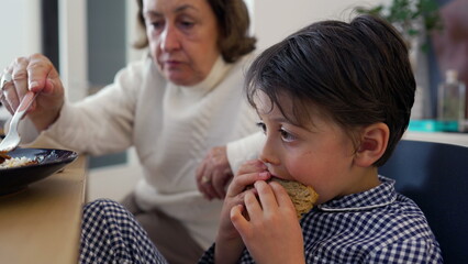 Young boy opens wide to be fed by grandmother, capturing the moment of trust and care during a meal at home. Strong bond between grandparent and child in a comfortable, loving environment