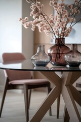 Stylish glass dining table with wooden base and pink chair, decorated with glass vases and dried flowers