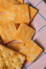 Square rosemary saltine crackers and square pieces of colby jack cheese on purple and blue grid pattern plate