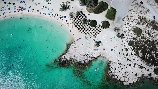 Aerial view of a beach full of tourists enjoying a sunny summer day, swimming in the turquoise water. An exotic beach of a sunny island and travel destination for summer vacations