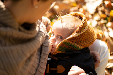 Obraz premium Blonde baby with blue eyes breastfeeding in a park