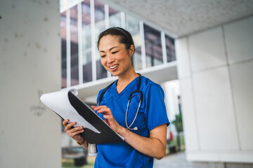 mature japanese doctor stand in front the building and hold clipboard