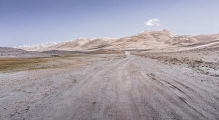Dusty road of the Pamir Highway winds and twists in the valley of the Tien Shan mountains in Tajikistan in Pamir, landscape in the high desert mountains for background