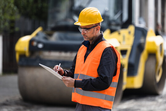 Construction worker in safety gear reviewing plans during roadwork at a construction site in the early afternoon