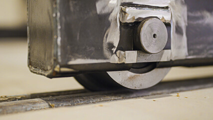 This image shows a close-up of a heavy-duty industrial metal wheel or roller mechanism moving along a rail, highlighting the robust engineering and wear on the components.