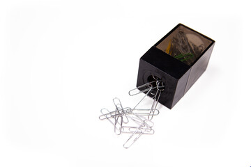 close-up of a black paperclip holder with paper clips spilling out against a white background