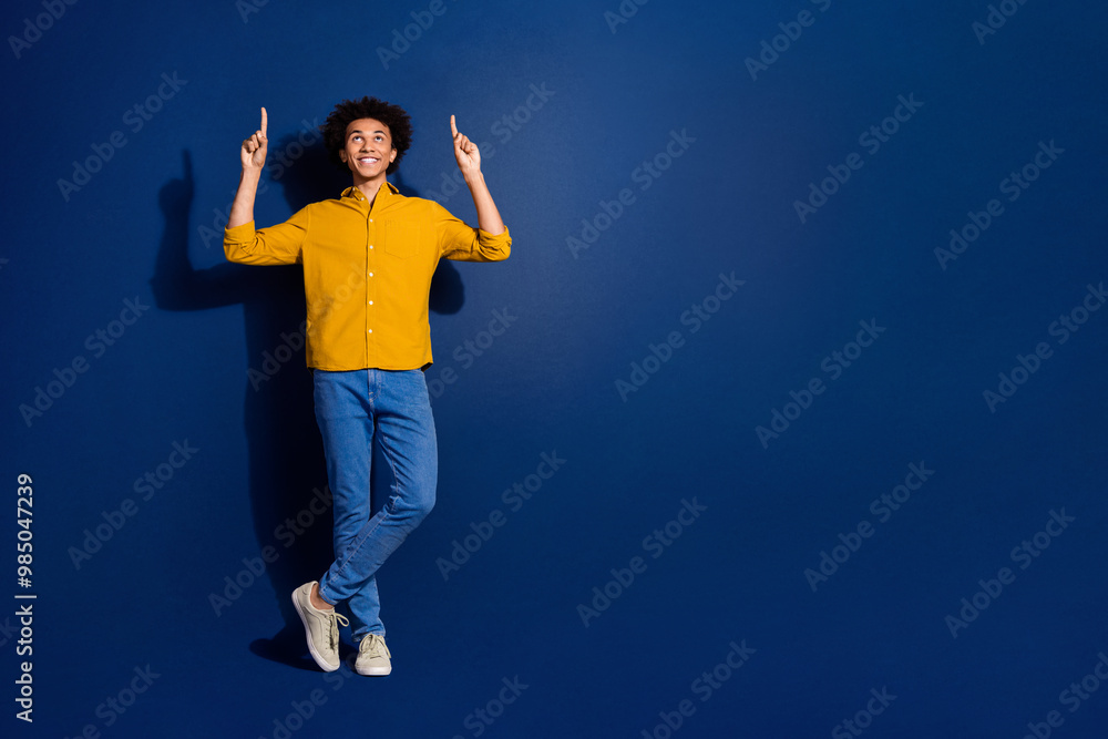 Wall mural Full body portrait of nice young man point fingers up empty space wear yellow shirt isolated on dark blue color background