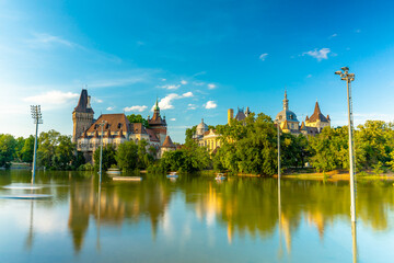 Obraz premium Budapest, Hungary - June 19, 2024: Vajdahunyad Castle during golden hour time. Moving catamarans in the pond on the foreground. Sunny summer day, clear sky.