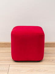 Square red pouf in living room. Vertical. Parquet floor and white wall