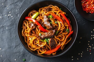 Stir fry noodles with vegetables and beef in black bowl. Slate background. Close up. Top view.