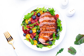 Foodie food salad with baked duck fillet, bloody oranges, kumquat, blueberries and mixed greens, white background, top view
