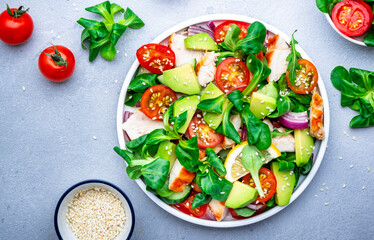 Fresh salad with avocado, chicken, tomatoes and lettuce, gray background, top view
