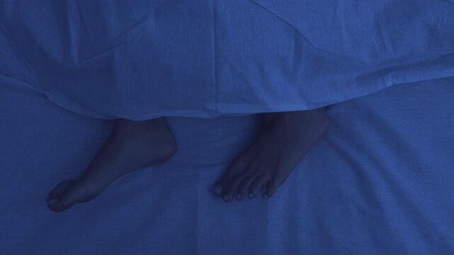 Comfortable sleep position. Feet of woman sleeping under duvet in bed at night, top view