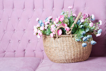 Wicker basket with a bouquet of flowers is on a velvet sofa. Congratulations background.
