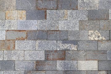 Texture of the sidewalk paved with gray rectangular stone tiles with brown stains as a background