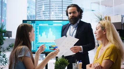 Financial advisor showing statistical graphs on big screen to customers, analyzing market trends to...