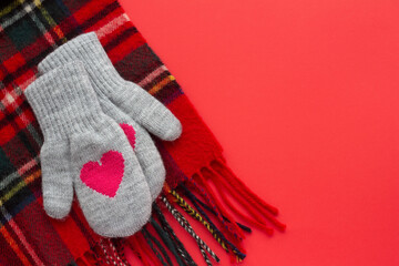 A pair of gray wool mittens with red hearts and knitted plaid scarf on red background. Winter clothing concept. Valentine's Day concept 