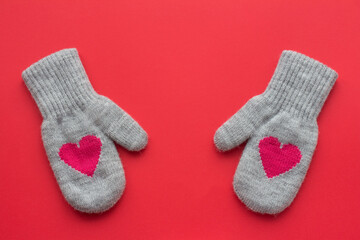 A pair of gray wool mittens with red hearts on a red background with copy space. Valentine's Day concept 