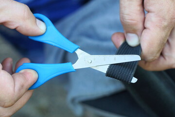iron sharp gray small with blue plastic handle industrial scissors in hand cutting black synthetic durable harness from bag  during the day on the street