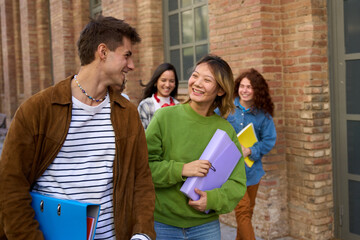 Couple of international happy university students walking together with positive expression. Group smiling young friends looking at each other in campus. Classmates colleagues and gen z relationships