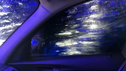 Automatic car washing in action view from the inside of car cabin. Blue brushes cleaning the windshield