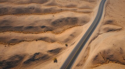 Fototapeta premium Aerial top view of desert road winding through dry landscape. Brown terrain stretches out to distant hill. Road narrow path, lined with stone structures in background. Scenic view of outdoors in