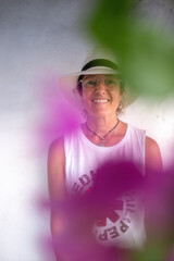 Portrait of a woman with white hat behind violet and pink flowers