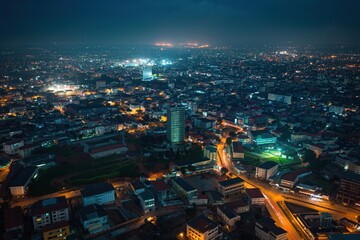 Aerial shot of Accra city at night, vibrant urban landscape with various buildings, roads. Cityscape with railway, bridges, streets, reflecting cultural, economic diversity. People, vehicles moving,
