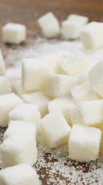 Granules of white sugar cubes fall into sugar sand, brown wooden surface. Unhealthy diet and food concept. Excess sugar impacts health. Emphasizes need for mindful eating and balanced nutrition