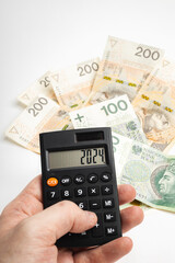 Calculator held in hand with the date "2024" in the background Polish PLN banknotes (selective focus)