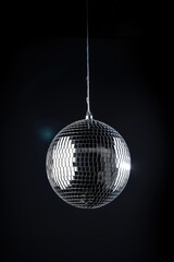 Shiny silver disco ball hangs isolated on dark black background. Bright reflective surface catches light, creating fun party atmosphere. Decorative lighting equipment for club, pub, or night events.