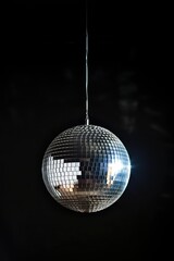 Obraz premium Shiny silver disco ball suspended vertically on dark black background. Close-up of metallic sphere with reflective surface. Glittering object for party decoration. Hanging equipment for night clubs,