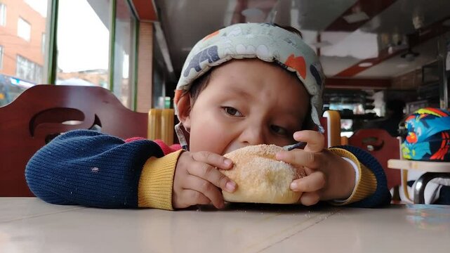 A Colombian child eats bread with a happy expression, enjoying the moment in a relaxed and homey setting.