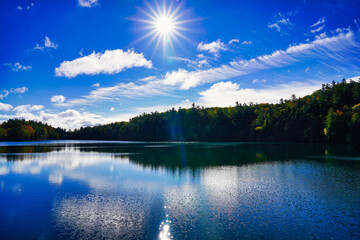 A bright overhead sun lights up the glass like surface of the scenic Pink lake, a meromictic lake situated in Gatineau Park,Quebec,Canada