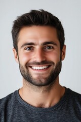 Obraz premium Young man with dark hair and a beard smiling against a plain background.