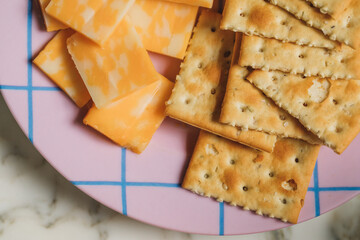 Square rosemary saltine crackers and square pieces of colby jack cheese on purple and blue grid pattern plate