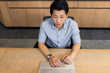 Working on laptop, asian man in office focusing on business tasks at desk