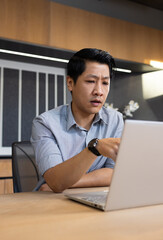 Working on laptop, asian man in office focusing on business tasks