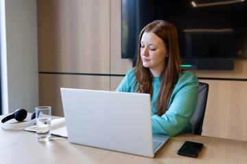 Working on laptop, woman in office with smartphone and glass of water nearby