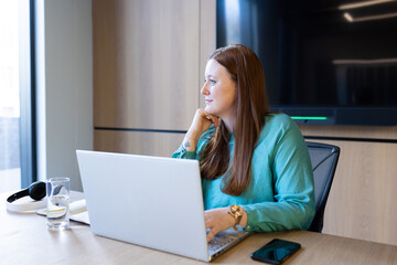 Working in office, woman using laptop and looking away thoughtfully