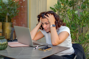 Young woman freelancer working with laptop at terrace table and talking on phone