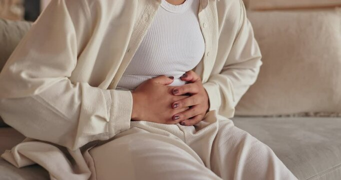 Stomach cramps, hands and woman on sofa in home with menstruation, periods or constipation. Tummy pain, sick and closeup of female person rubbing belly for IBS, endometriosis or virus in living room.