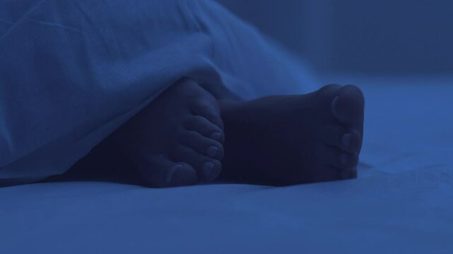 Woman sleeping in bed at night, beautiful female bare feet under white blanket closeup.