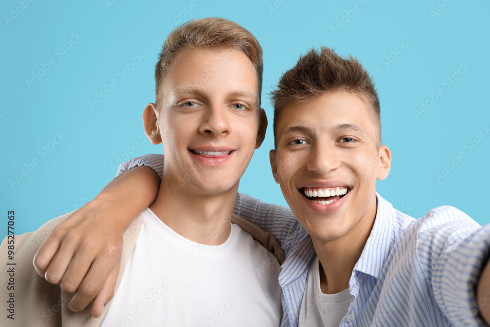 Poster happy brothers taking selfie on light blue background